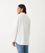 Camisa blanca de manga larga con cuello camisero, cierre frontal con botones a tono, dos bolsillos con solapa en el pecho y puños con trabilla.