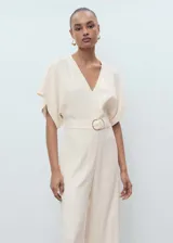 Mono largo color crema, con cuello de pico, manga corta y cinturón con hebilla. Cierre de cremallera en la parte posterior.