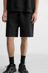 Bermuda negra relaxed fit confeccionada en tejido interlock de algodón con elasticidad. Cintura elástica ajustable con cordón. Bolsillos laterales y detalle de bolsillo trasero de plastrón.