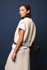 Chaleco de lana color crema, tejido a punto perlado con calado en la parte delantera. Tiene cuello a la base y silueta cuadrada.