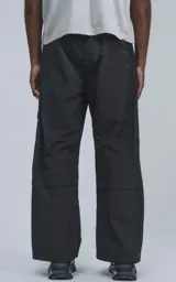 Pantalón cargo negro de silueta oversize, confeccionado en tejido técnico liviano de poliéster. Presenta múltiples bolsillos cargo con solapa y detalles reflectivos horizontales en la parte superior de los bolsillos.