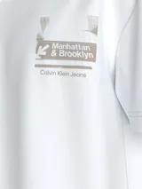 Remera blanca de algodón con cuello redondo y mangas cortas. Estampado gráfico en el pecho con el texto "Manhattan & Brooklyn" y el logo de Calvin Klein Jeans.