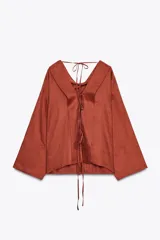 Blusa color ladrillo confeccionada en lino 100%. Tiene cuello fluido, mangas largas acampanadas y espalda descubierta ajustable con cordones.