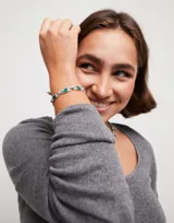 Pulsera rígida plateada con eslabones rectangulares que contienen cristales verdes esmeralda. Incluye cierre de mosquetón y dije con el logo de la marca Uno de 50.