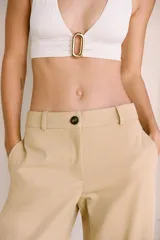 Pantalón color beige de tiro alto con bolsillos delanteros y falsos bolsillos de vivo en la espalda, de pierna ancha y corte recto. Cierre frontal con cremallera y botón.