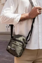 Morral color verde oliva con correa ajustable negra, cierre superior con cremallera, bolsillo frontal con cremallera y parche con texto "NOT JUST A BAG".