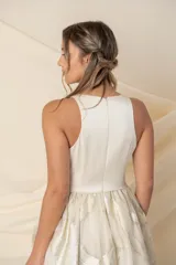 Vestido largo de fiesta color champagne, con corpiño tipo corsé de crepe de seda y falda amplia de organza con lurex dorado. Incluye bolsillos laterales.