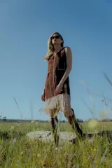 Vestido corto marrón de gamuza sintética, sin mangas, con escote en V y detalle de flecos en el ruedo. Presenta apliques bordados en el frente y laterales.