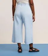 Pantalón tipo pantacourt de jeans en tono delavê, con corte amplio y largo a media pantorrilla. Presenta cintura con elástico en la espalda, cierre frontal con botón forrado, bolsillos laterales tipo cuchillo y pliegues delanteros.