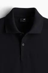 Remera polo negra de piqué de algodón, de corte estándar, con cuello clásico, tapeta de botones, mangas cortas y remate acanalado en cuello y mangas.