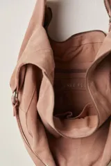 Bolso tipo hobo de gamuza negra, con forma holgada y cierre principal de cremallera. Se lleva al hombro con dos asas de correa delgadas sujetas con argollas metálicas plateadas.