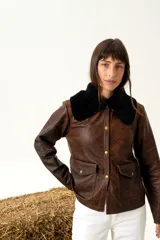 Chaqueta marrón de cuero con cuello de piel sintética negra, cierre con botones a presión, bolsillos con solapa y corte a la cintura.