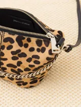 Bandolera confeccionada en cuero con estampado animal print, detalles en cuero vacuno y cadena metálica plateada en el frente. Tiene correa regulable de cuero y bolsillo interno con cierre.