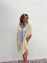 Vestido camisero beige de lino con cuello y solapa azul lavanda, cierre frontal con botones y mangas largas.