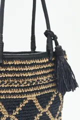 Bolso tote tejido en raffia color negro y beige, con vivos y correas en cuero sintético negro. Tiene cierre interno con snap metálico y forro de algodón.