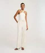 Pantalón de vestir color crudo, de corte recto, con bolsillos laterales y traseros. Se ajusta a la cintura con cinturón de cuero marrón con hebilla dorada.