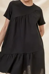 Vestido negro corto con cuello redondo, mangas cortas y falda con volantes.
