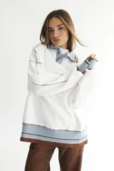 Buzo celeste con cuello polo y puños en rib color verde lima. Tiene un parche con el logo de la marca en el pecho y rayas horizontales en el ruedo.