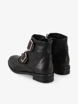 Botín de cuero negro con doble hebilla decorativa y punta redondeada.