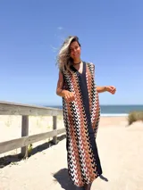 Vestido largo tejido con patrón geométrico en tonos marrón, beige, blanco y negro. Tiene escote en V y corte holgado.