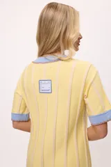 Vestido de tejido de punto, color negro con rayas verticales grises. Tiene cuello redondo y puños y ruedo en color rojo con costuras decorativas en hilo azul. Presenta un pequeño bordado de una letra 'B' estilizada en el pecho.