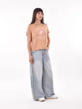 Remera color tostado con estampa frontal que incluye texto y dibujo de una surfista.