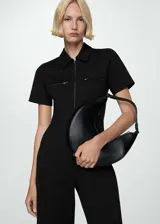 Mono largo negro de tejido fluido con diseño entallado, cuello polo, manga corta, cierre frontal con cremallera y dos bolsillos con cremallera en la parte frontal.