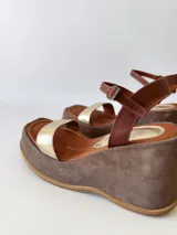 Sandalias de cuero con plataforma, color marrón con tira dorada sobre los dedos y tobillera marrón con hebilla.