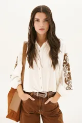 Camisa blanca de manga larga con bordados florales marrones en las mangas.