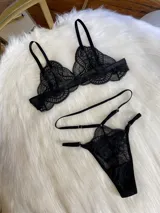 Conjunto de lencería negro de encaje, compuesto por un corpiño tipo bralette, una tanga de tira doble regulable, un portaligas desmontable y ligas regulables.