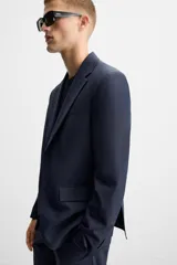 Blazer azul marino con sutil diseño de cuadros, corte regular fit, cuello con solapas de muesca, manga larga con puños abotonados, bolsillo de vivo en el pecho, bolsillos de solapa en la cadera, bolsillo interior, aberturas en la espalda y cierre frontal con dos botones.