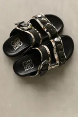 Sandalias bajas de cuero marrón con doble tira, hebilla ajustable y apliques de tachas metálicas.