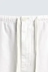 Pantalón negro de corte relajado y pierna ancha, confeccionado en mezcla de algodón y lino. Presenta cintura elástica ajustable con cordón y cierre frontal con cremallera y botón.