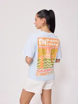 Remera negra de algodón con corte holgado y estampado frontal con el texto "Rusty Australia Mermaid Beach" en colores naranja, verde y amarillo.