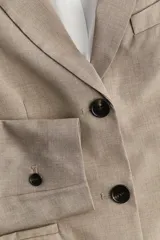 Blazer color beige de corte entallado, con solapas de muesca, bolsillo superior insertado y bolsillos delanteros. Modelo con hombreras, botonadura frontal, botón decorativo en los puños y abertura atrás.