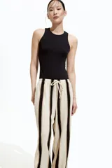 Pantalón de punto color crema con rayas verticales negras y marrones, de corte holgado y tiro alto, con cintura elástica y cordón ajustable.