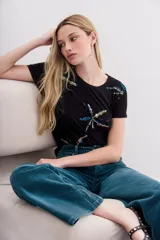 Remera negra de algodón con cuello redondo y mangas cortas. Presenta un estampado de palmeras con lentejuelas y canutillos de colores.