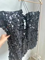 Vestido corto negro con lentejuelas de distintos tamaños, tirantes finos elastizados y cierre en la espalda.