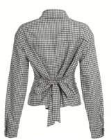 Camisa de manga larga con estampado a cuadros pequeños en tonos blanco y negro/gris. Presenta un escote pronunciado en V por botones desabrochados y un detalle fruncido o ajustado en la cintura que marca la silueta.