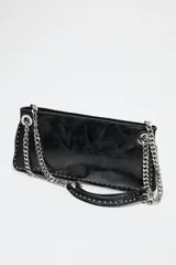 Bolso alargado negro con tachas plateadas en el borde inferior y detalle de cremallera en el corte. Tiene asa de cadena plateada multiposición para usar al hombro o como bandolera. Incluye bolsillo interior con cremallera y cierre principal con cremallera.
