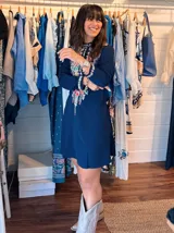 Vestido corto blanco con bordado floral multicolor en el frente, escote redondo con cierre de cremallera parcial y mangas largas.