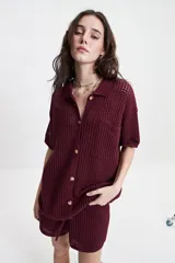 Camisa tejida color borgoña con textura calada, cuello clásico, botones y mangas cortas con elástico.