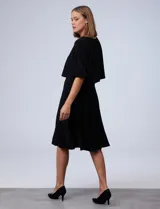 Vestido midi negro con corte a la rodilla, de seda fría, con capa superior superpuesta y mangas cortas.