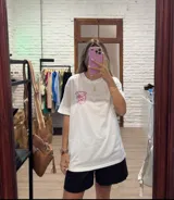 Remera blanca de corte holgado con cuello redondo y manga corta. Presenta un pequeño estampado frontal con texto en rosado y un limón cortado.