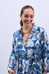 Vestido estilo camisola con estampado floral en tonos azules y marrones, con cuello camisero, mangas largas con puños y cierre frontal con botones. Incluye cinturón de la misma tela.
