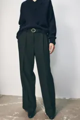 Pantalón negro de tiro alto con pinzas delanteras, pernera ancha y cinturón de cuero con hebilla dorada.