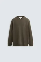 Jersey color verde oliva, de corte boxy, tejido en hilatura con mezcla de algodón y cashmere. Tiene cuello redondo, manga larga y acabados en rib.