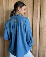 Camisa a rayas verticales color beige y blanco, de corte holgado, con cuello con volados, cierre parcial con botones y mangas largas con puños abotonados.