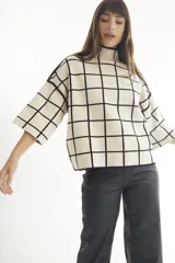 Sweater color crema con cuello alto y mangas cortas anchas, con diseño de cuadros negros.