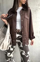 Sobrecamisa marrón de gamuza sintética, corte oversize, con cuello camisero, cierre frontal con botones a presión, mangas largas con puños abotonados, bolsillos de parche en el pecho y detalle de calado con motivos florales en el ruedo.